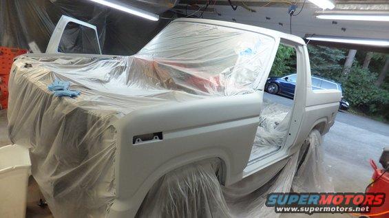 White 1980s Ford Bronco in primer, doors open, covered in plastic sheeting