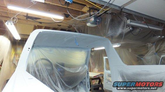 1983 Ford Bronco body covered in plastic, interior visible, in a garage with paint prep lighting