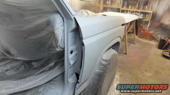 White Ford Bronco body in primer, door open, covered in plastic sheeting, in a workshop