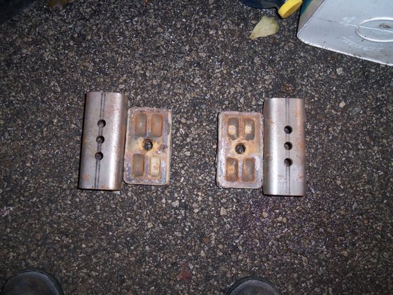 Two pairs of metal suspension components on asphalt