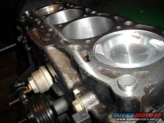 Engine block with four cylinders, showing wear and some damage. A sensor is attached to the side