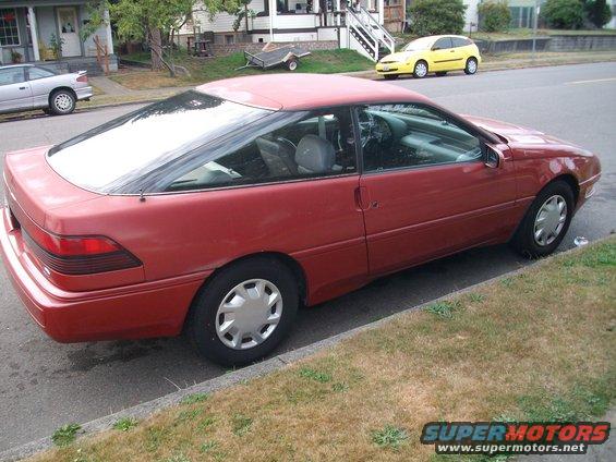 Red 1989 Ford Probe coupe parked curbside, showing its side and rear quarter panel