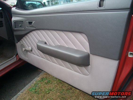 Car door panel with gray fabric insert and armrest. Vent and window crank visible