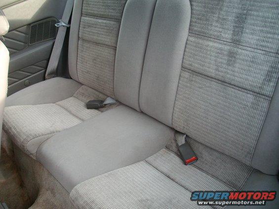 Rear bench seat with grey patterned fabric and seatbelts. Visible speaker grille on the left