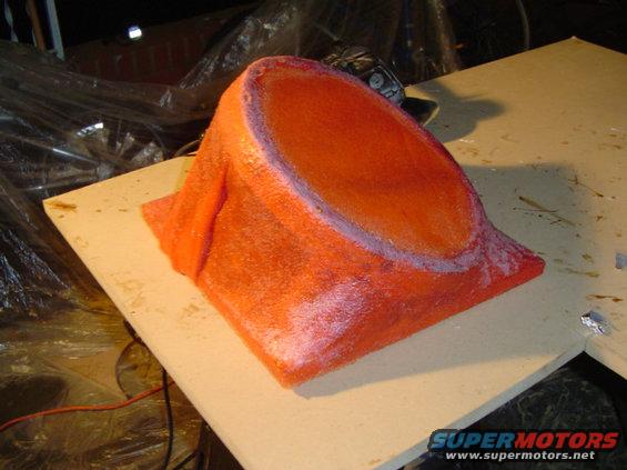 Orange foam mold for a custom car speaker enclosure, sitting on a wooden surface