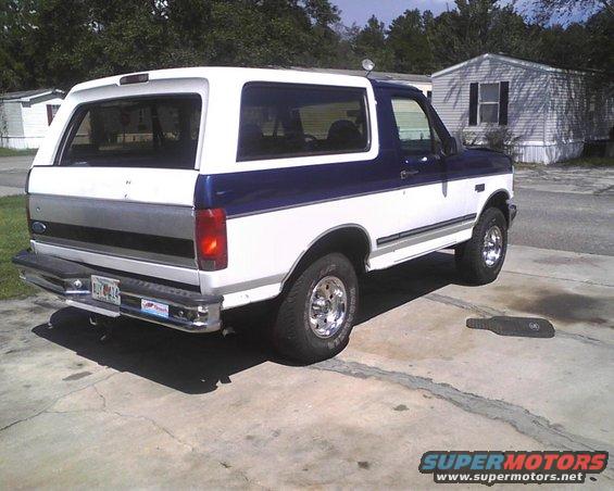 White and blue Ford Bronco parked on concrete, rear quarter view