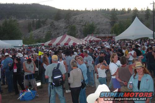Crowd at an outdoor event with tents and hills in background
