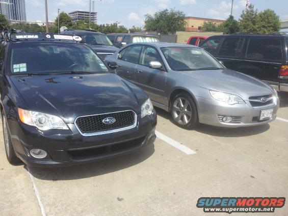 Front view of a black Subaru Legacy wagon with a Yakima rack, parked next to a silver Subaru Legacy sedan