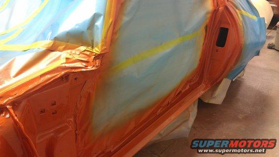 car door masked off for painting, showing orange primer and blue masking film