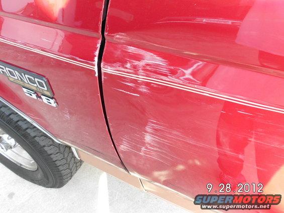 Red 1994 Ford Bronco side panel with extensive scratches and dents
