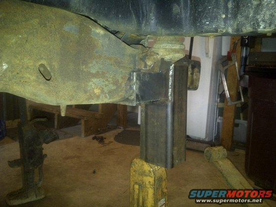 Welded steel bracket attached to rusty vehicle frame, supported by jack stands