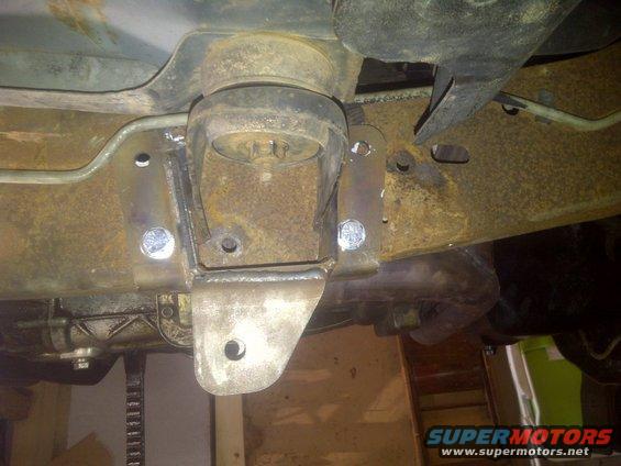 Close-up of a rusty vehicle frame with a newly welded, custom suspension bracket and bolts