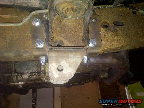 Custom suspension bracket bolted to rusty frame, with exhaust pipe visible