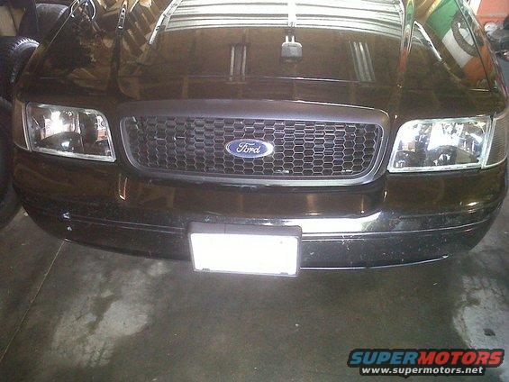 Front view of a black Ford Crown Victoria with a honeycomb grille and Ford badge. Headlights are visible