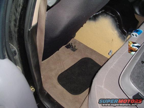 Car interior floor with tan carpet and black floor mat, showing part of a seat and door frame
