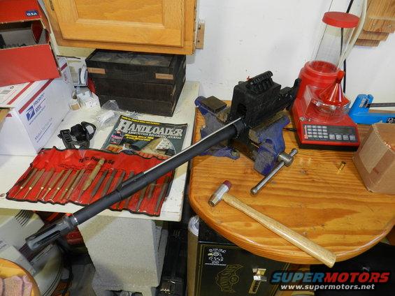 Workbench with a gun barrel in a vise, reloading scale, and tool set