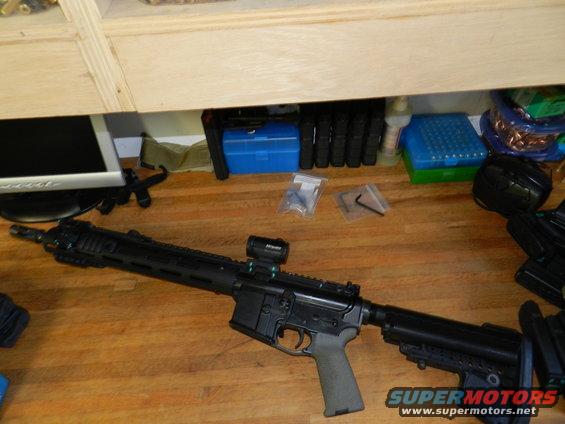 AR-15 rifle with red dot sight, magazines, and tools on a wooden surface