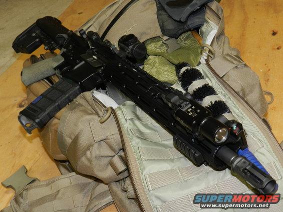 Black assault rifle with red dot sight and flashlight resting on tan tactical gear
