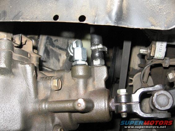 Power steering gearbox with hoses and belt. Text reads 'SUPERMOTORS.NET'