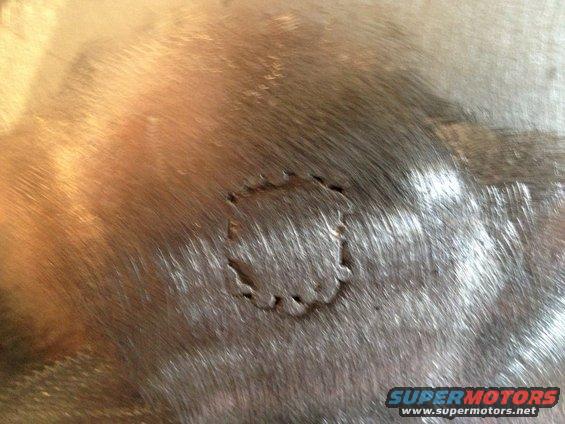 Close-up of a metal panel with a rough circular cutout and some scratches