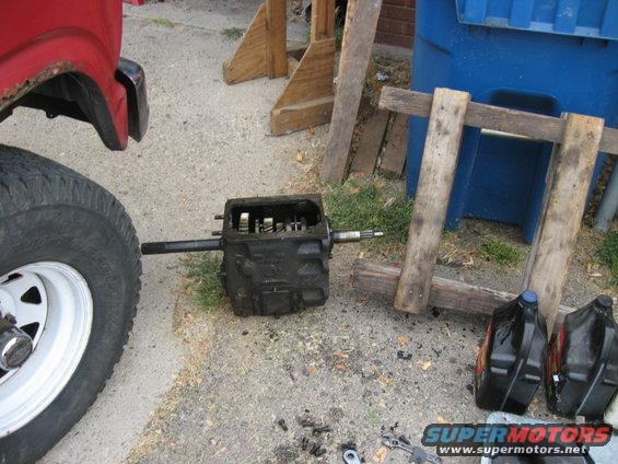 Removed transmission and loose parts on the ground next to a red vehicle's tire