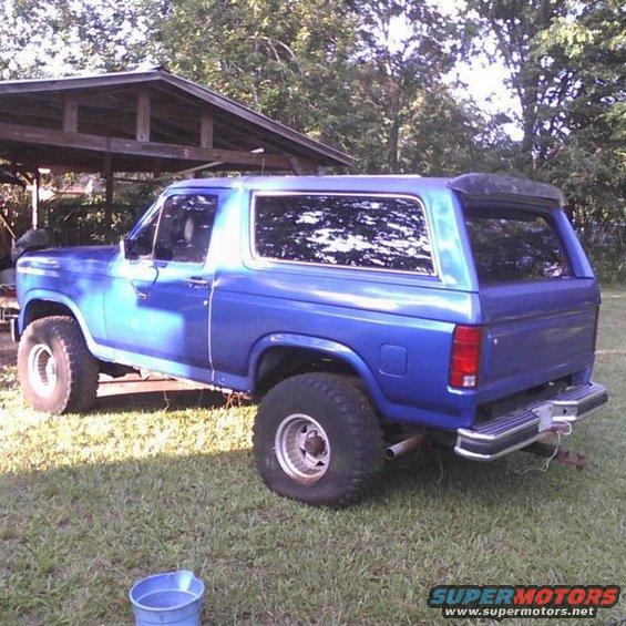 Blue Ford Bronco parked on grass next to a wooden shelter