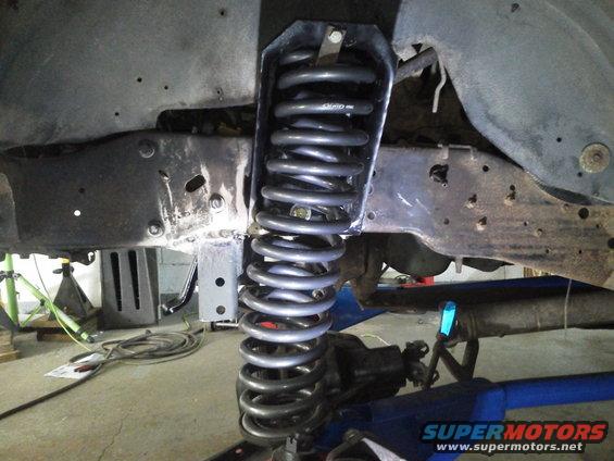 Close-up of a vehicle's front suspension with a large coil spring and heavy-duty frame components