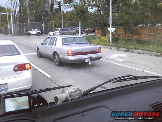 Silver Lincoln Town Car with a trailer hitch driving on a street, seen from another car