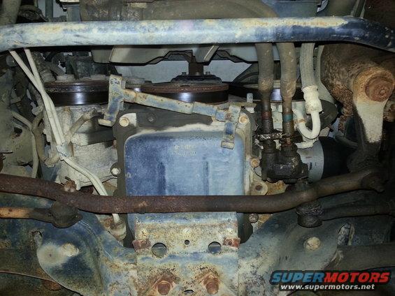 Underside view of vehicle engine parts, showing belts, pulleys, and some hoses