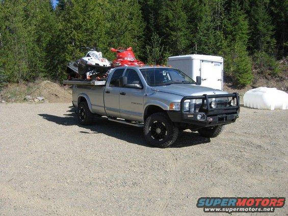 2005 Dodge 3500 pickup truck with two snowmobiles loaded on a flatbed in a gravel lot