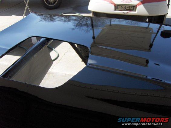 Black car hood with a large scoop opening, reflecting trees and a golf cart