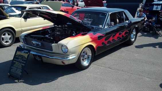 Classic Mustang with flames painted on the side, hood open showing the engine. Another car is parked next to it