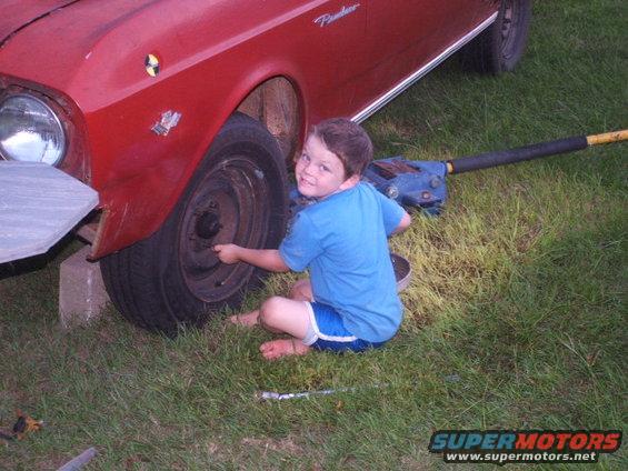 1966 Ford Ranchero with a boy in blue shorts and shirt working on the front wheel