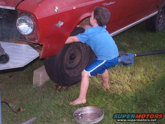 Boy changing tire on red 1966 Ford Ranchero, jacked up with concrete blocks