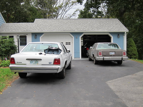 White sedan with a black tarp on its trunk, parked in a driveway