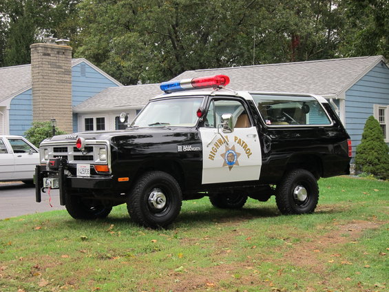 Black and white police SUV with "HIGHWAY PATROL" text on door, parked on grass