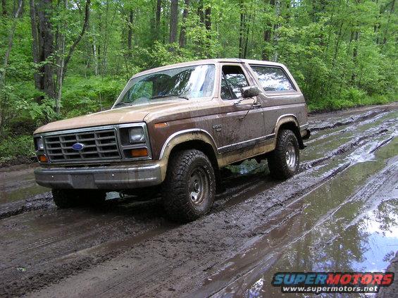 Brown Ford Bronco on a muddy forest road, front 3/4 view