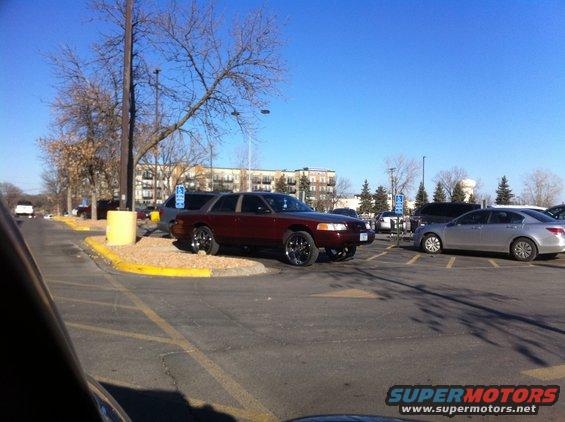 Maroon sedan with chrome rims parked in a lot. Another car is parked next to it