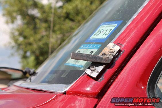 Close-up of a red vehicle's windshield with a metal bracket attached and inspection stickers visible
