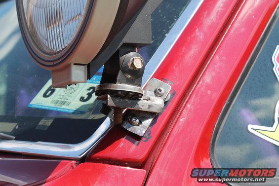Close-up of a red vehicle's A-pillar showing a mounted auxiliary light and a sticker on the window