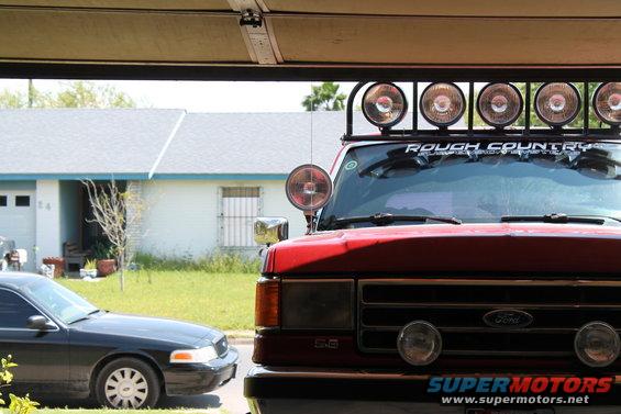 1990 Ford Bronco front end with Rough Country light bar and a black sedan parked nearby