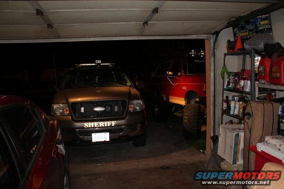 Sheriff SUV front view with light bar, red pickup truck behind