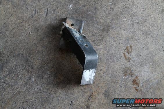 Metal bracket with white paint on its lower section, lying on a concrete floor