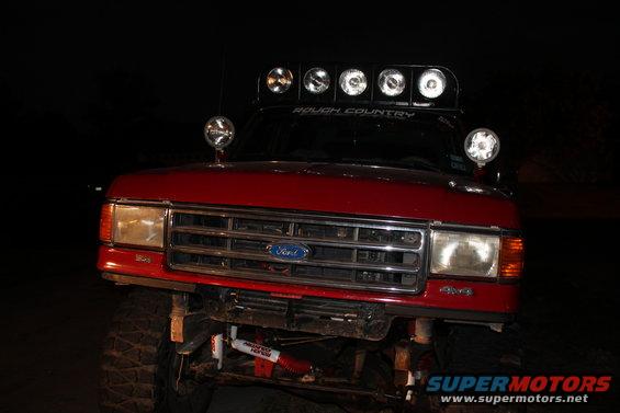 Front view of red Ford truck with 'Rough Country' light bar and '4x4' badge. It has a winch and off-road shocks