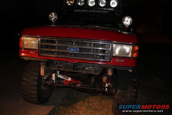Red Ford truck front view, modified with off-road lights and suspension