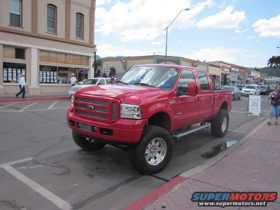Red Ford F-Series truck with chrome wheels and side steps parked on a street