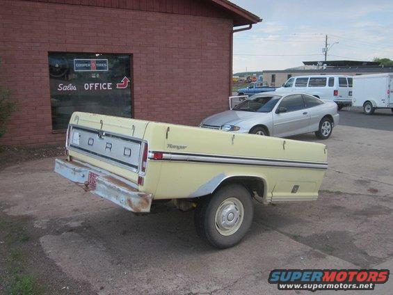 Yellow Ford pickup truck, rear view. "Ranger" badge visible on fender. "Cooper Tires" and "Sales OFFICE" signs on building