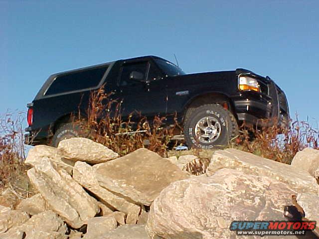 1995 Ford Bronco climbing over large rocks with dry grass and blue sky