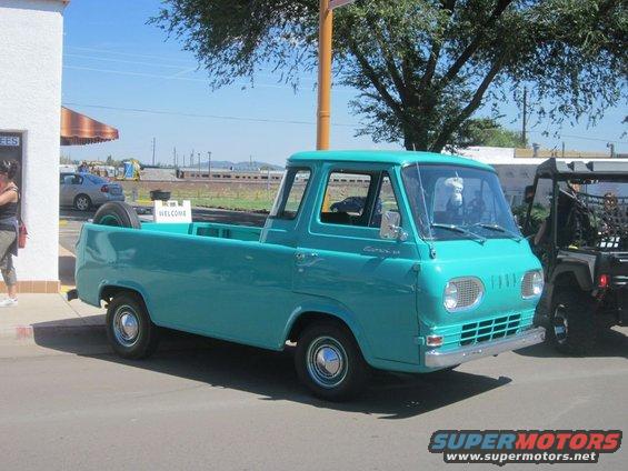 Turquoise 1961 Ford Econoline pickup truck parked next to a black utility vehicle