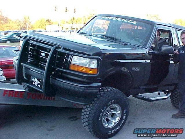 Black Ford Bronco with a bull bar and skull decal, on a trailer. "FORDZILLA" sticker on windshield